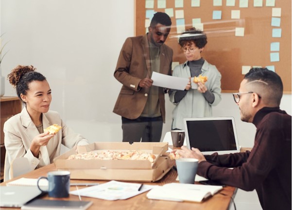 A team of four people collaborate together in the office with a box of pastries on the table
